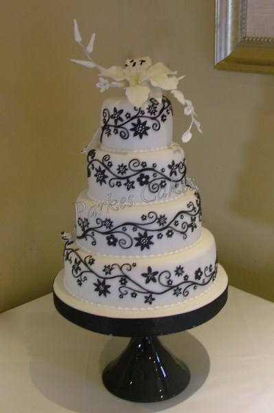 four tier white wedding cake with black applique flowers and scrolls