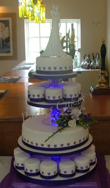 four tier wedding cake with purple hearts and mni cakes